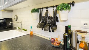 Una cocina con salpicadero de azulejos blancos, un lavamanos de acero inoxidable y varios utensilios de cocina colgados en un colgador.