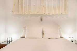 Un lit avec une literie blanche, une table de chevet avec une lampe et un luminaire fixé au mur.