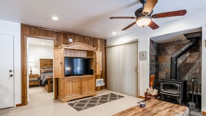 Una sala de estar acogedora con un mueble de madera para entretenimiento, una chimenea y un ventilador de techo.