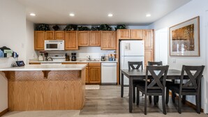 Una cocina moderna con armarios de madera, microondas, lavavajillas y una zona de comedor con mesa y sillas.