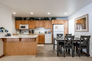 A modern kitchen with wooden cabinets, a microwave, a dishwasher, and a dining area with a table and chairs. - Hidden Valley Village #103 nicely updated 1 bedroom 1 bathroom condo short 10 min walk from Village (Mammoth Lakes)