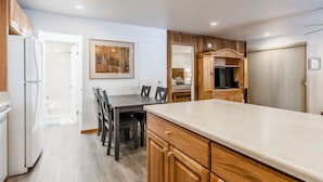 Una cocina moderna con armarios de madera, una mesa de comedor con sillas, un refrigerador y un televisor.