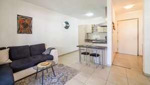 En moderne stue med en sofa, et lille sofabord og et spiseområde med stole samt et køkken i baggrunden.