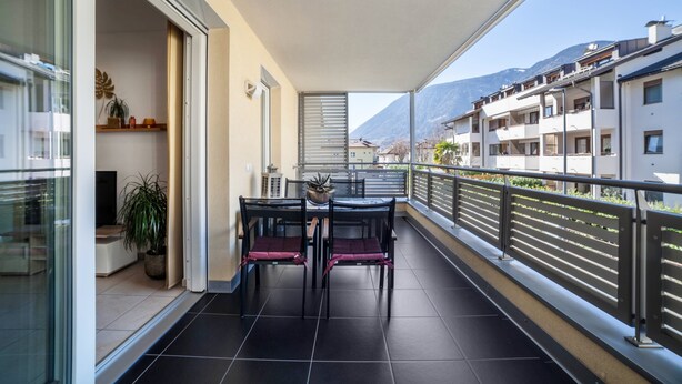 En balkon med et bord og stole, en potteplante og udsigt til bygninger og bjerge.
