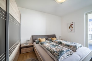 A bedroom with two beds, a nightstand, a bedside table, a wall-mounted artwork, and a window.