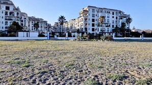Un edificio grande con varios balcones y techo plano, rodeado de un área verde con palmeras.