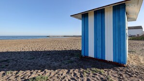 Una playa con una pequeña estructura azul y blanca, arena y el océano al fondo.