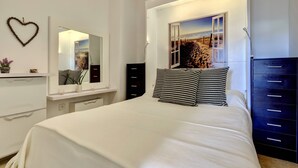 Un dormitorio con cama, cómoda, espejo, decoración con forma de corazón y una vista a la playa a través de la ventana.