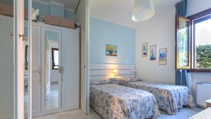 Una camera da letto con due letti, un armadio, una finestra con tende e un quadro appeso al muro.