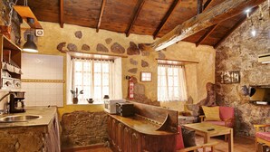 Une cuisine rustique avec des murs en pierre, des poutres en bois, un comptoir de bar et un évier en pierre.