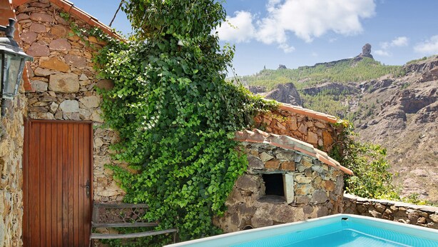 Un bâtiment en pierre avec une porte en bois, un mur de pierre recouvert de lierre et une piscine à l’eau cristalline.