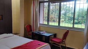 Quarto de hotel com uma cama, uma escrivaninha e uma cadeira. Há uma janela com vista para o verde lá fora.