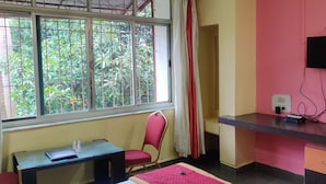 Quarto com escrivaninha, cadeira, televisão e janela com vista para o verde.