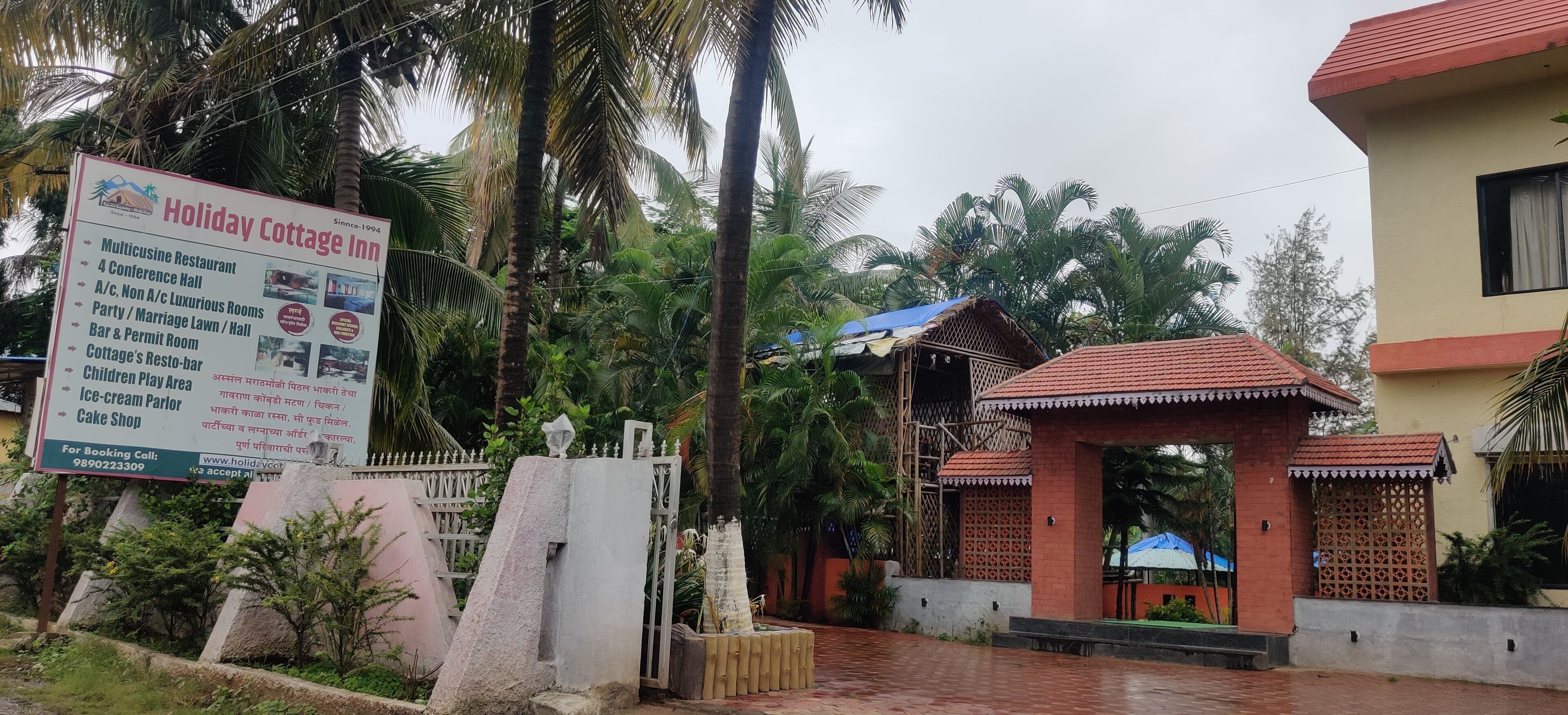A Holiday Cottage Inn signboard listing amenities like a multicuisine restaurant, conference hall, and children's play area.