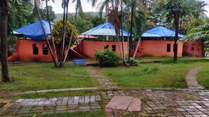 Um espaço ao ar livre rústico com construções de telhado vermelho, um caminho pavimentado e vegetação exuberante.