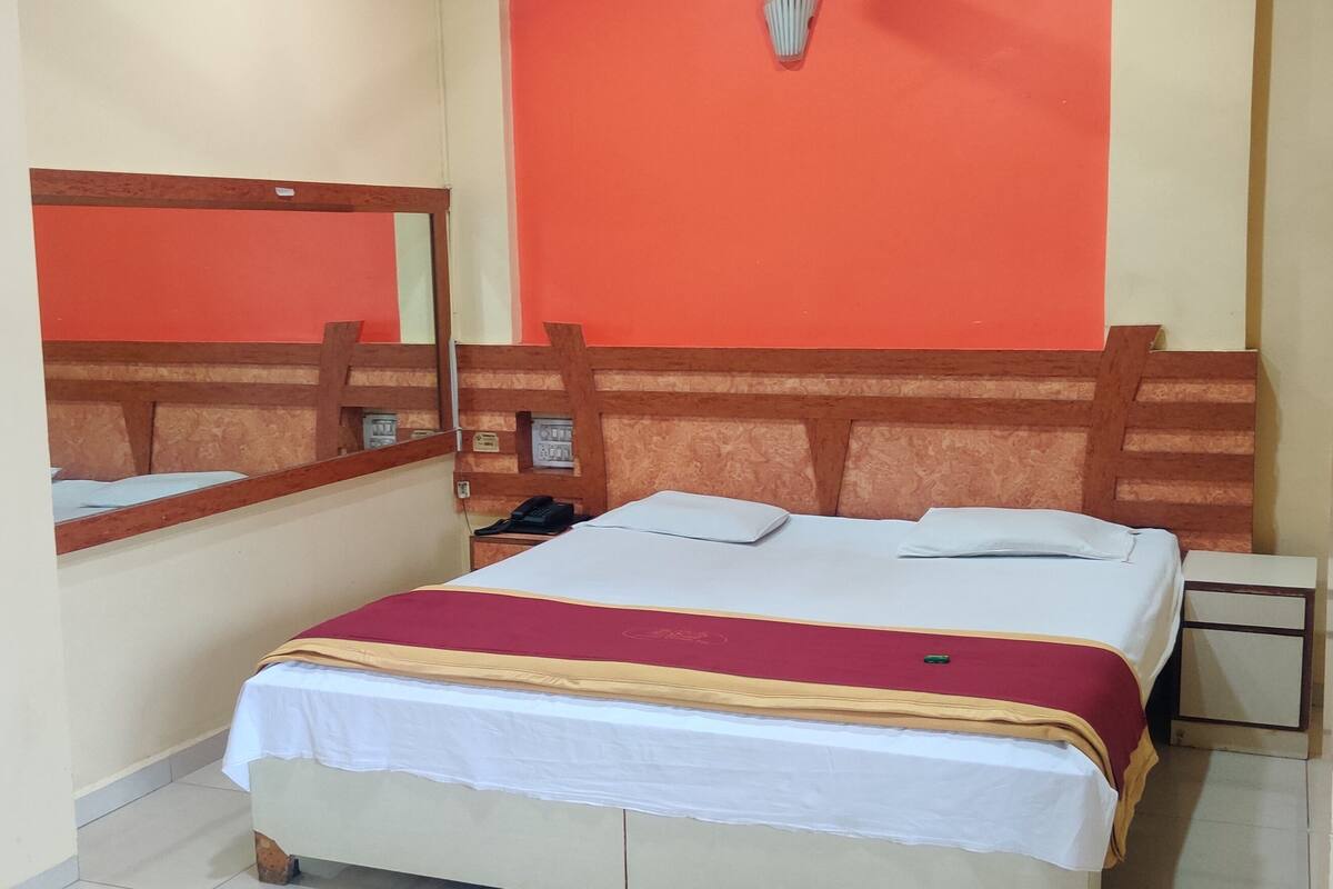 A hotel room with a bed, bedside tables, a mirror, and a red accent wall.