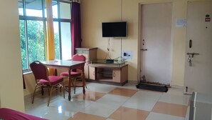 Quarto com uma cama, uma escrivaninha com computador, televisão e janela com cortinas.