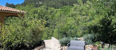 Eine Terrassenfläche mit Gartenmöbeln und Grill, umgeben von viel Grün und einem Bergpanorama.