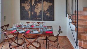 Un comedor con una mesa preparada para cuatro personas, un mapa del mundo en la pared y una escalera con barandilla de metal.