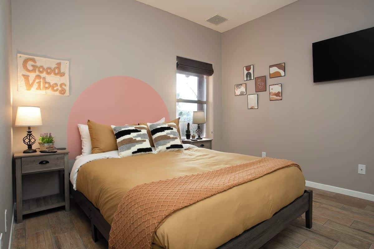 Un dormitorio con cama, mesitas de noche, televisor montado en la pared y ventana con vistas.