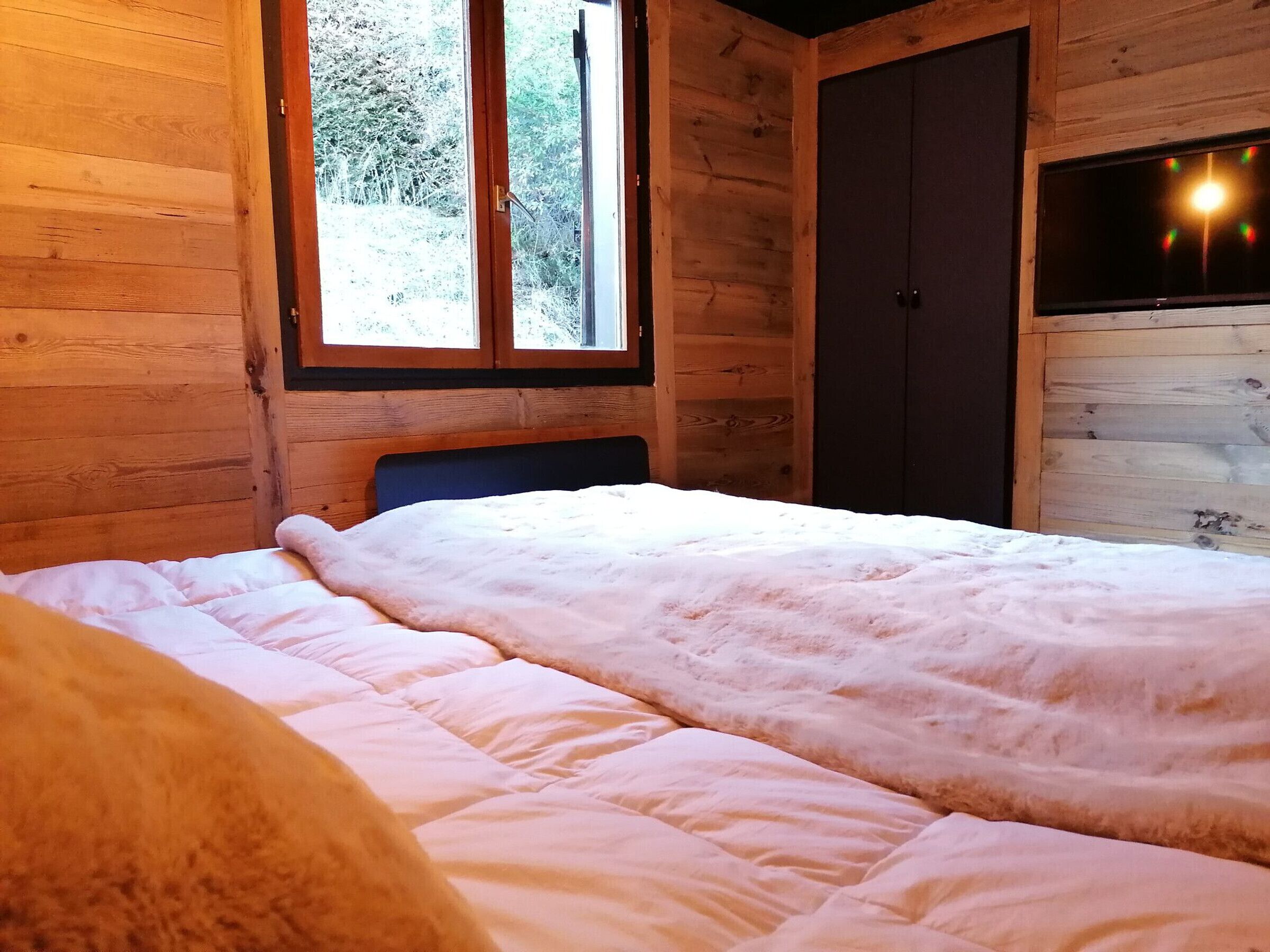 Una habitación de cabaña de madera con una cama, un ventanal y una puerta.
