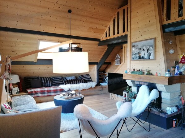 A cozy wooden cabin interior with a loft bed, a fireplace, and a dining area.
