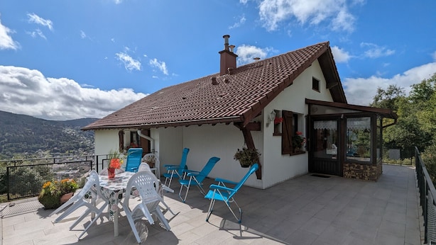 A house with a tiled roof, a patio with chairs and a table, and a view of the mountains.