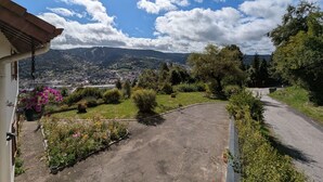 A residential area with a paved driveway, a garden with flowers, and a view of a town and mountains in the distance.