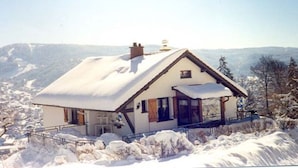 A snow-covered house with a sloped roof, a chimney, and a balcony.