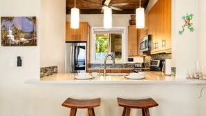A modern kitchen with a central island, stainless steel appliances, wooden cabinets, and pendant lighting. - 🏖️Oceanfront Penthouse w/ AC + Pickleball + Views (Kailua Kona)