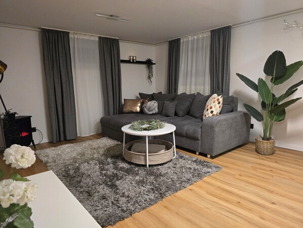 Ett modernt vardagsrum med en grå soffa, ett runt soffbord och en stor krukväxt.