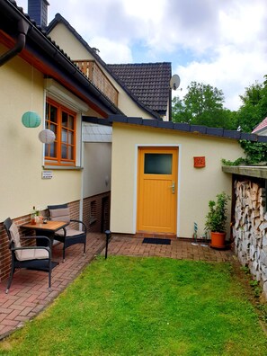 Une maison avec une porte en bois, une terrasse en briques et un petit jardin.
