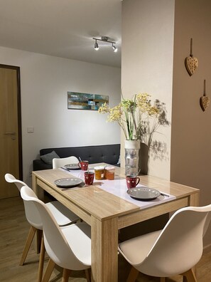 Un comedor con una mesa de madera, sillas blancas, un florero con flores y un cuadro en la pared.