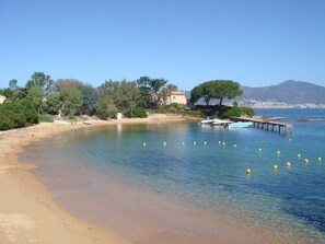 Uma praia costeira com águas cristalinas, areal arenoso e um cais com barcos.