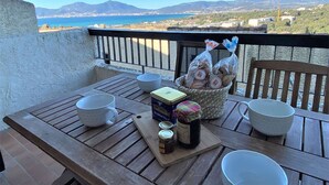 A wooden table with breakfast items and a view of the sea and mountains.
