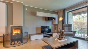 A modern living room with a fireplace, a flat-screen TV, a sofa, and a dining area with chairs.