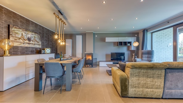 A modern living room with a sofa, a dining area with chairs, a fireplace, and a TV.