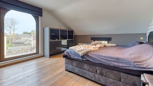 A bedroom with a large window, a bed, a wardrobe, and a desk.