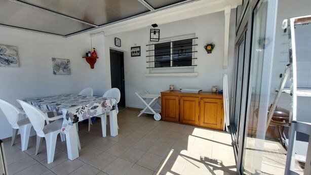 Ein Essbereich mit Tisch und Stühlen, eine kleine Küchenzeile mit Spüle und Schränken sowie ein Fenster mit Jalousien.