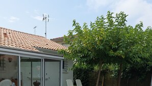 Ein überdachter Außenbereich mit Kiesboden, einem Baum und einem Gebäude mit Ziegeldach.