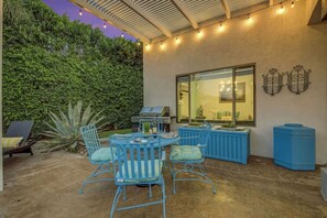 An outdoor patio with a dining table and chairs, a grill, and a large window. - Terra Azul: Pool, Spa, Billiard Table, Foosball (Indio)
