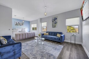 A modern living room with a sofa, a coffee table, and a bed with a blue accent wall. - Terra Azul: Pool, Spa, Billiard Table, Foosball (Indio)