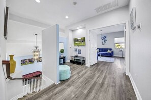 Un pasillo amplio con una escalera que conduce a una sala de estar, un sofá azul y un televisor.