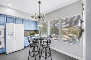 A modern kitchen with blue cabinets, a glass dining table, and a unique ceiling light fixture. - Terra Azul: Pool, Spa, Billiard Table, Foosball (Indio)