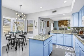 Una cocina moderna con armarios azules, encimera de granito y un comedor con mesa de vidrio y sillas negras.