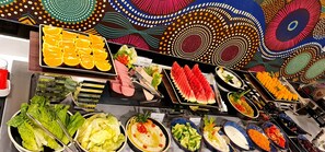 Un buffet proposant une variété de plats, notamment des tranches d’orange, de la pastèque et différentes sortes de salades.