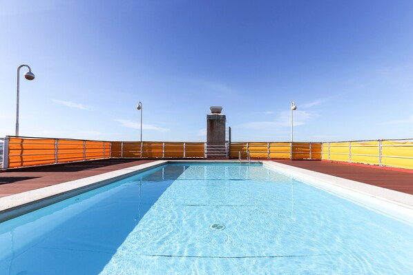 A swimming pool with a clear blue water surface, surrounded by a red deck and orange safety barriers.