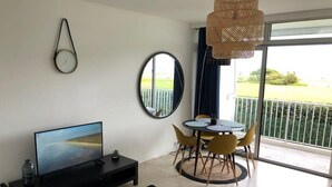 Een moderne woonkamer met een flatscreen televisie, een eethoek met gele stoelen, een ronde tafel en een balkon met uitzicht.