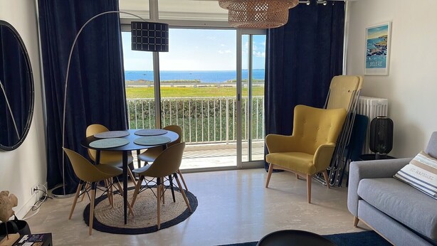 Een kamer met balkon, een eettafel met stoelen, een bank en een stoel.