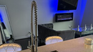 A modern kitchen with a stainless steel sink, a high chair, and a flat-screen TV mounted on the wall.
